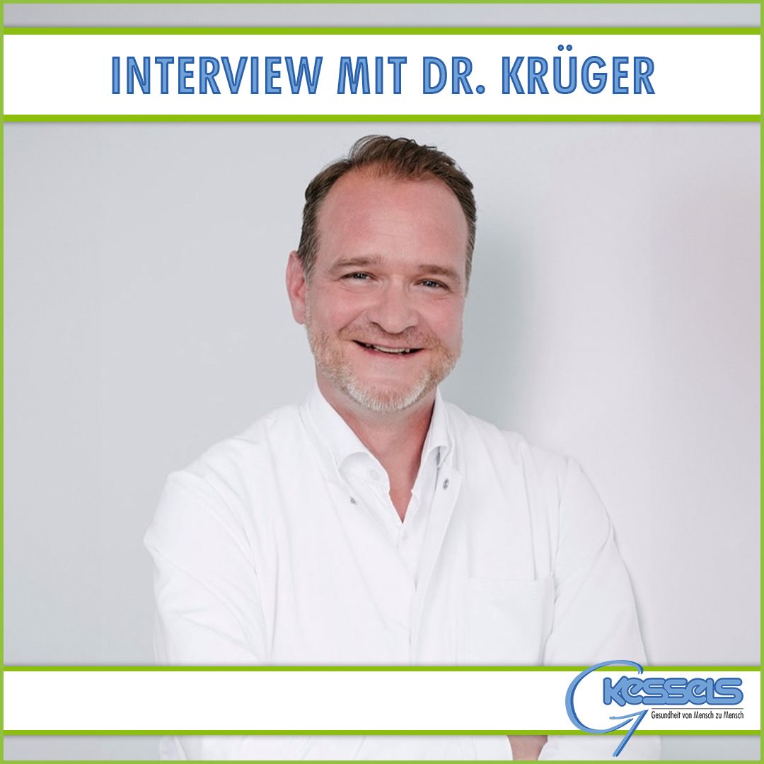 Ein Mann in einem weißen Laborkittel steht mit verschränkten Armen vor einem hellgrauen Hintergrund, auf dem der Text: Interview mit Dr. Krüger steht.