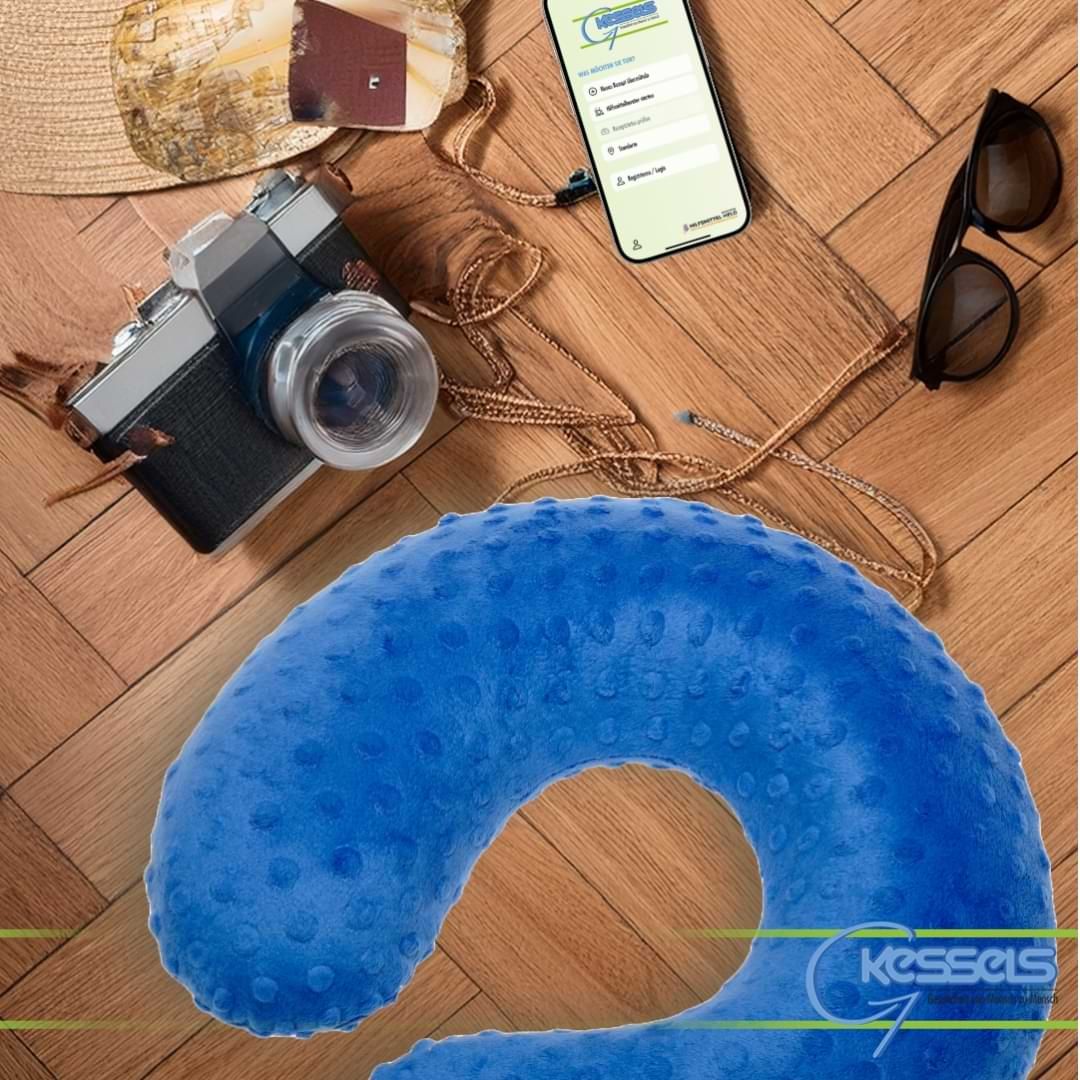 Ein blaues Nackenhörnchen mit Noppenstruktur im Vordergrund; im Hintergrund liegen Reiseutensilien wie eine Kamera, Sonnenbrille und ein Smartphone auf Holzparkett.