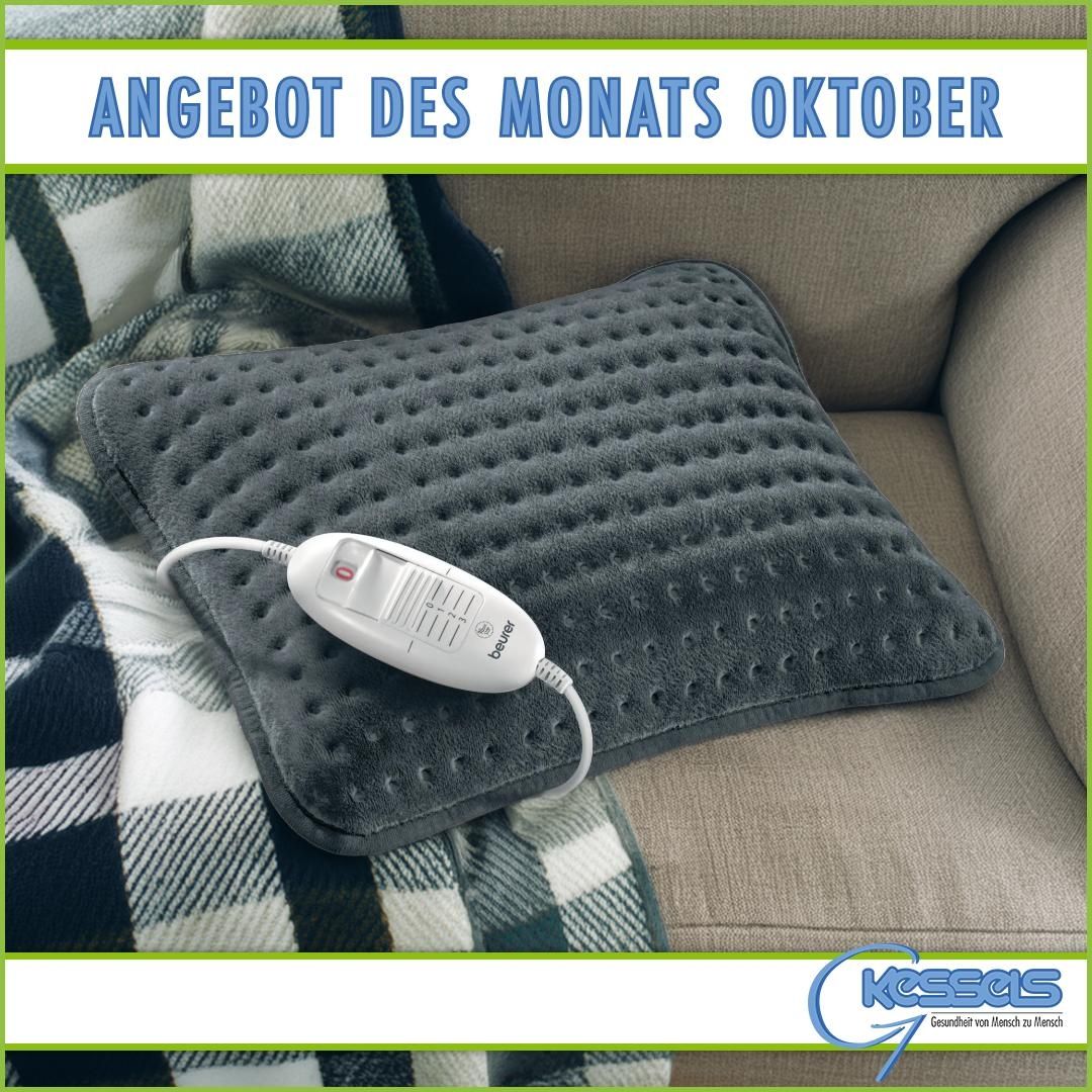 Ein weiches, graues Heizkissen mit Steuereinheit liegt auf einem gemütlichen Sofa, daneben eine karierte Decke. Der Text lautet: Oktober-Angebot